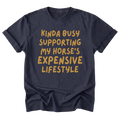 A navy blue t-shirt featuring the text 'KIDNA BUSY SUPPORTING MY HORSES'S EXPENSIVE LIFESTYLE' printed on the front in gold color.
