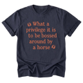 A navy blue short-sleeve t-shirt with a warm orange graphic text print on the front that reads 'What a privilege it is to be bossed around by a horse' flanked by two small leaf icons, displayed on a clean white background.