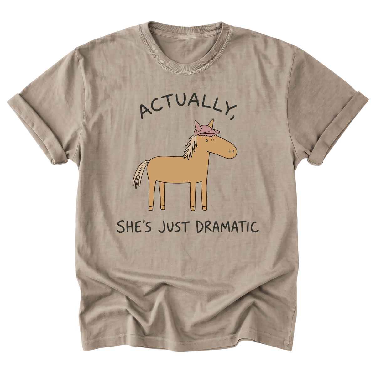 A sand beige short-sleeve t-shirt with a graphic of a cartoon horse wearing a pink bow and the text 'ACTUALLY, SHE'S JUST DRAMATIC' printed on the front, displayed against a solid white background.