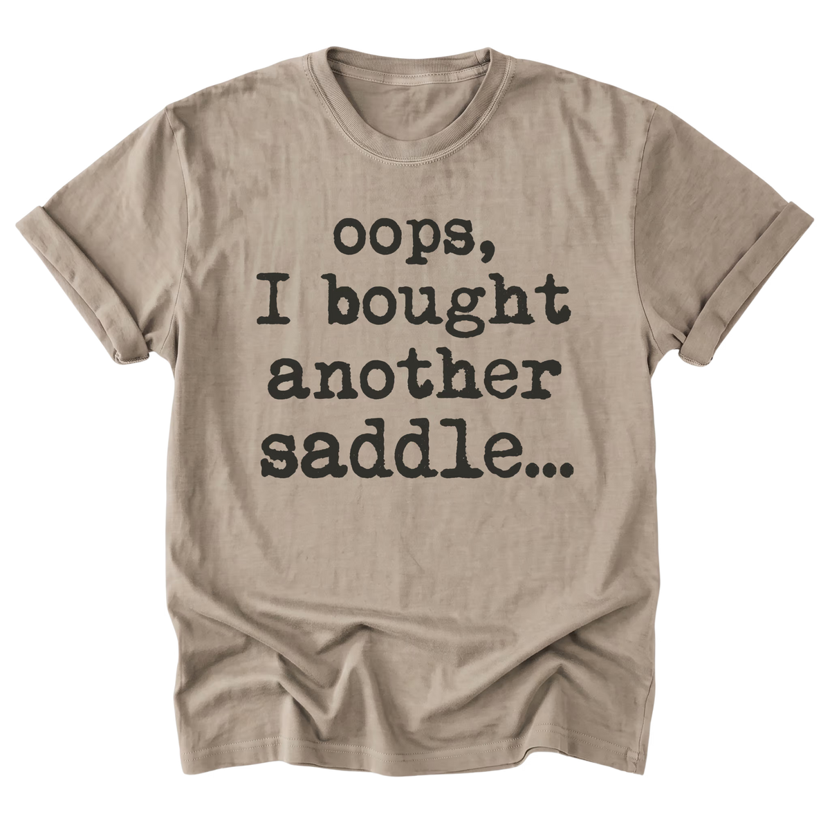 A sand brown t-shirt with a dark gray typewriter-style text print that reads 'oops, I bought another saddle.