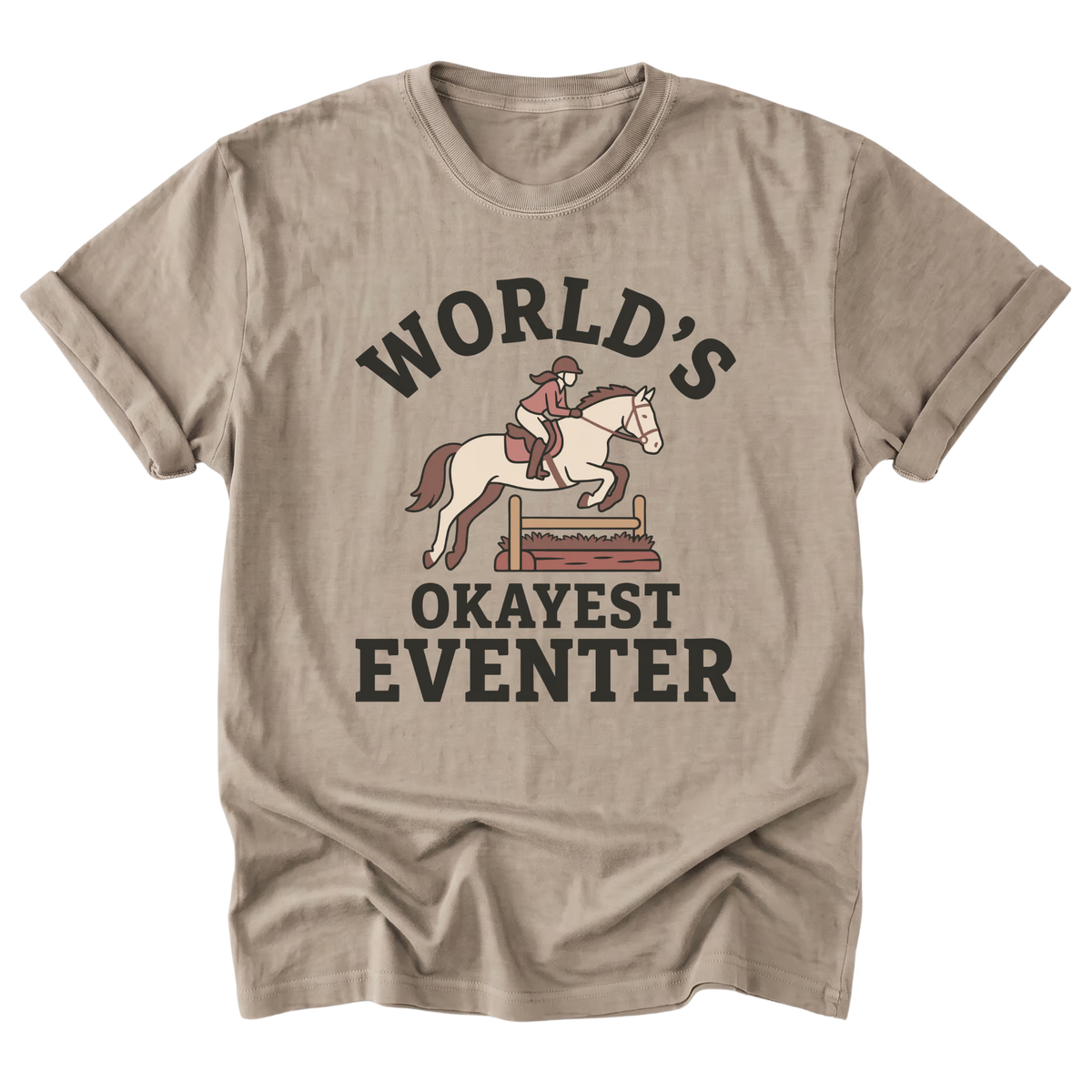 A sand beige short-sleeve t-shirt with a graphic print of a horse rider on a white horse jumping a fence, with the text 'WORLD'S OKAYEST EVENTER' in dark brown lettering.